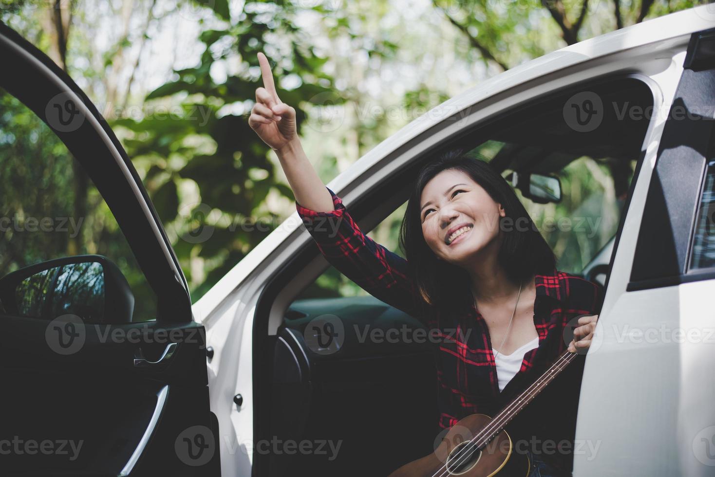 mulher asiática de beleza apontando e se divertindo no verão ao ar livre com ukulele no carro branco. viagem do conceito de fotógrafo. estilo moderno e tema de mulher solo. estilo de vida e tema de vida de felicidade foto