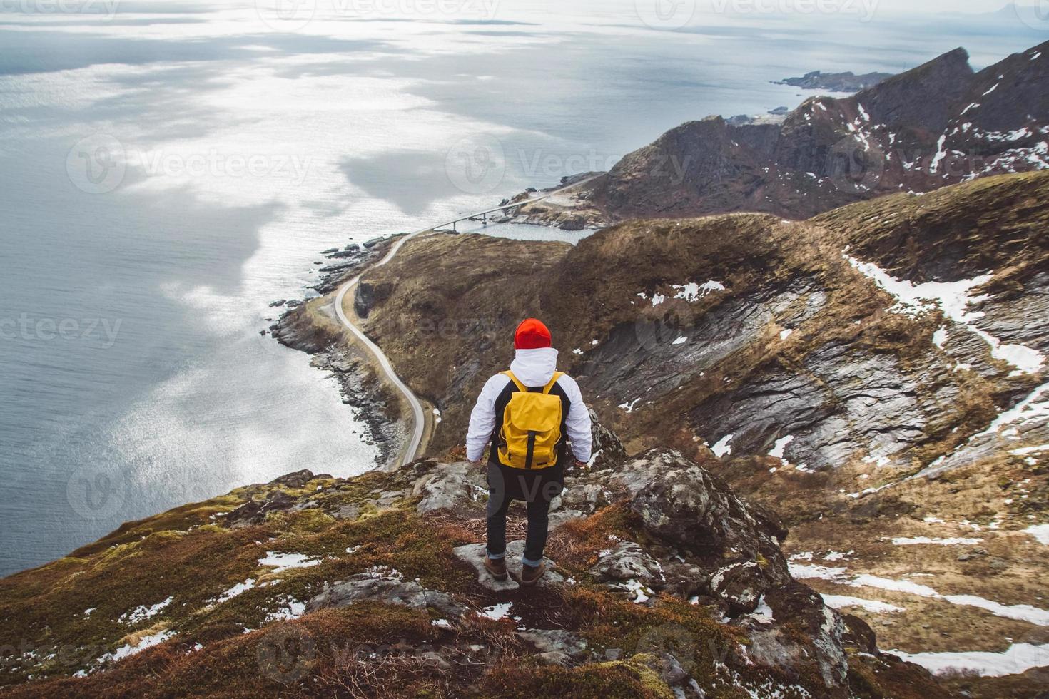 homem viajante com uma mochila amarela de pé nas rochas contra o fundo do mar e das montanhas foto