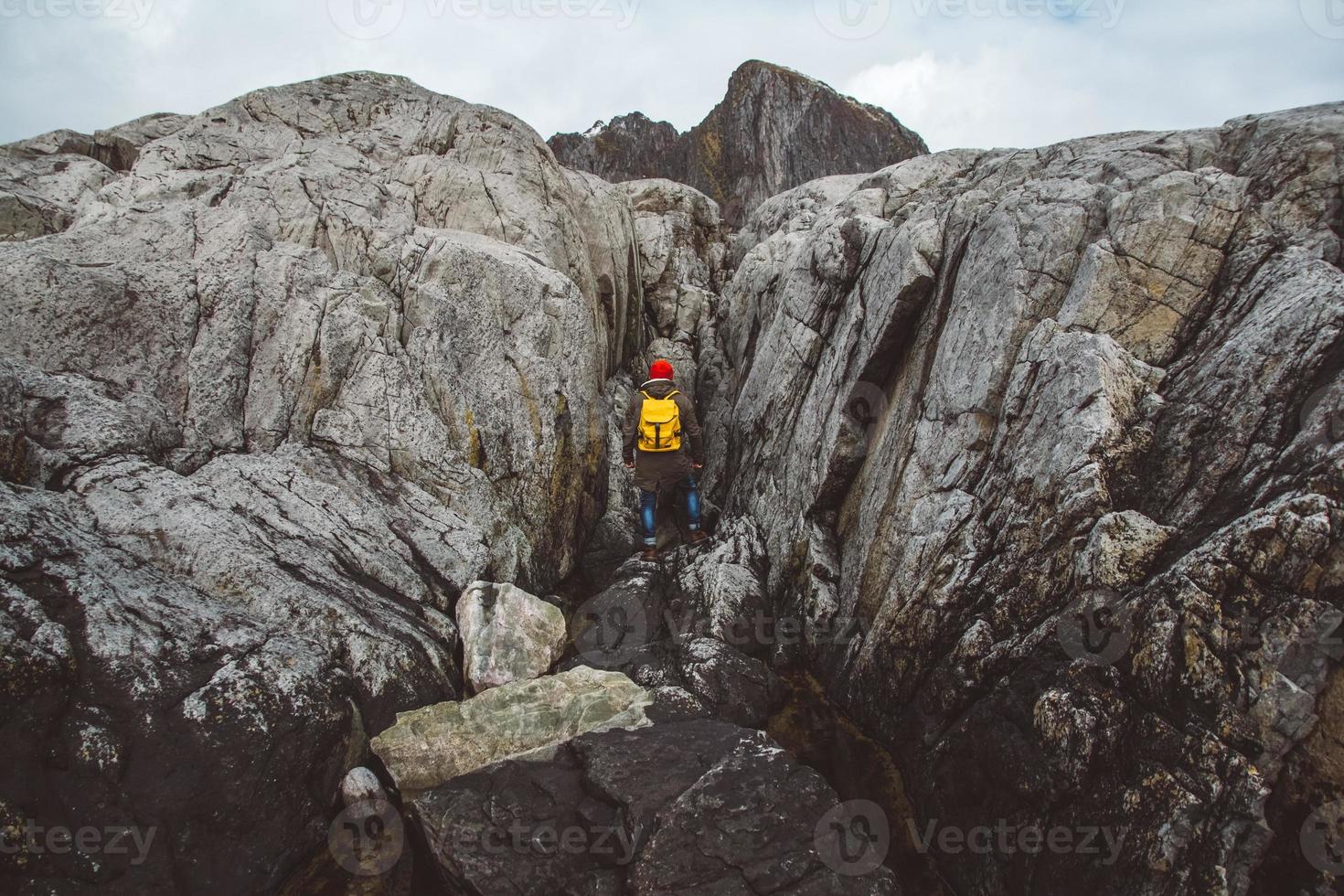 homem viajante com uma mochila amarela com um chapéu vermelho em pé no fundo das rochas. conceito de estilo de vida de viagens. atirar pelas costas foto