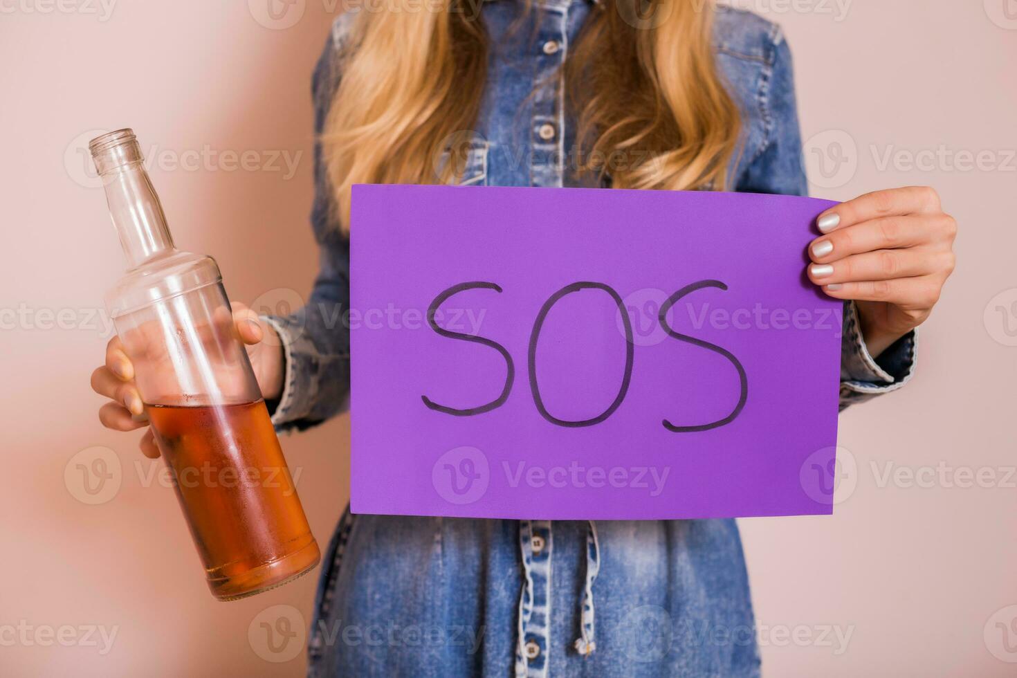 mulher segurando álcool e papel com palavra SOS enquanto em pé dentro frente do parede.desistir bebendo álcool conceito. foto
