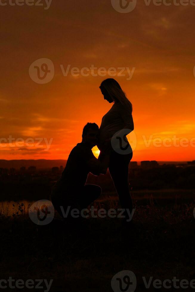 silhuetas do marido ouvindo barriga do dele grávida esposa enquanto elas apreciar gastos Tempo juntos ao ar livre.toned imagem. foto