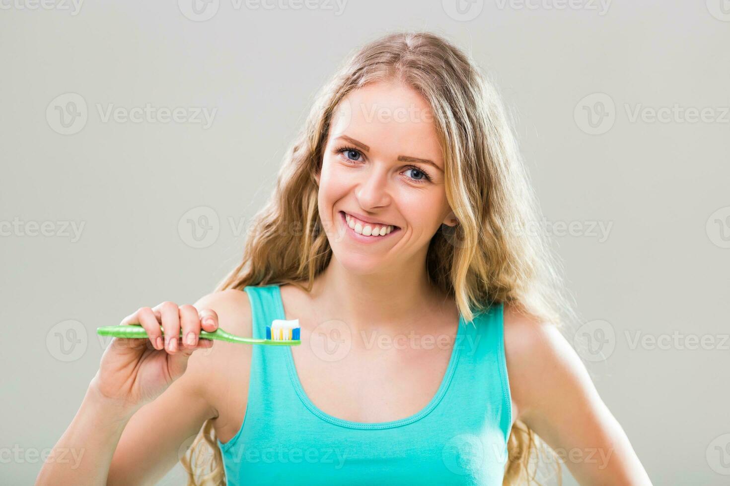 lindo jovem mulher escovar dentes em cinzento fundo. foto