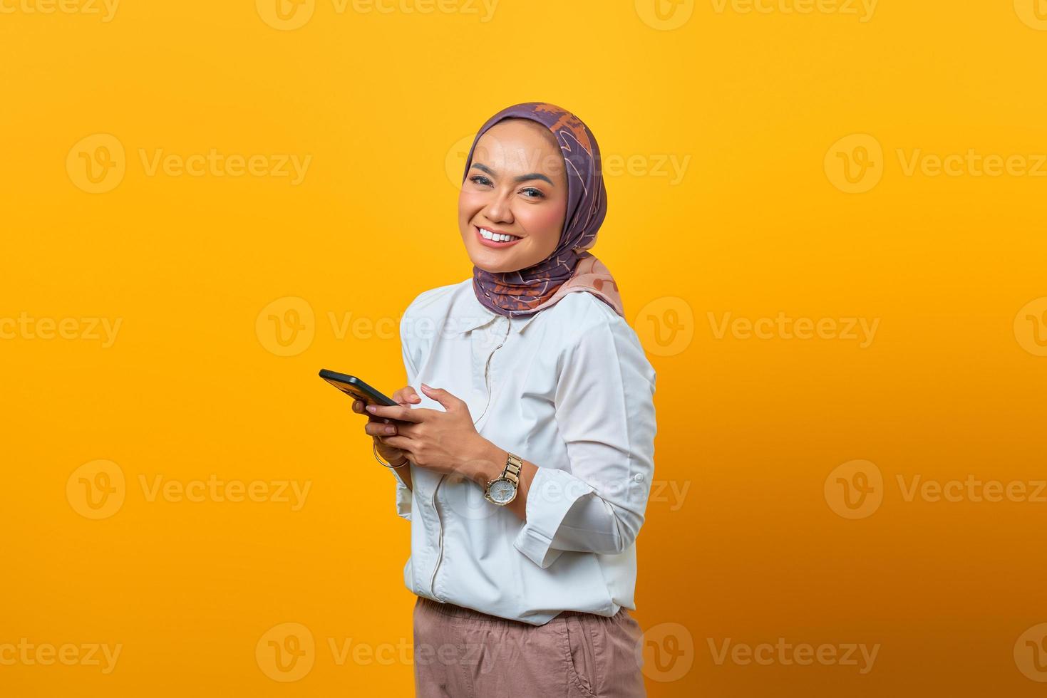 mulher asiática alegre usando o celular e olhando para a câmera foto