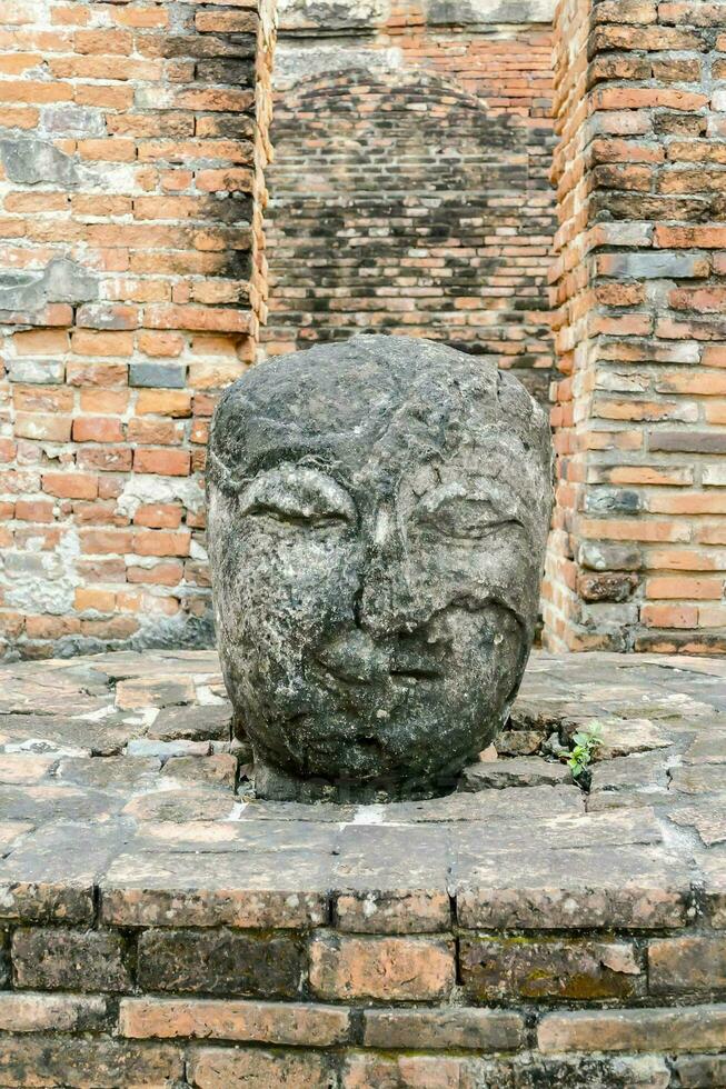 uma pedra face sentado em uma tijolo parede foto