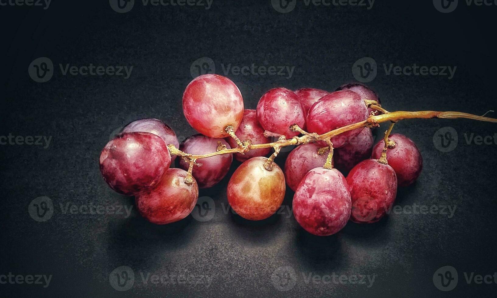 uma raminho do uvas estava fotografado com a conceito do dando uma luz efeito para a uvas isolado em uma Preto fundo foto