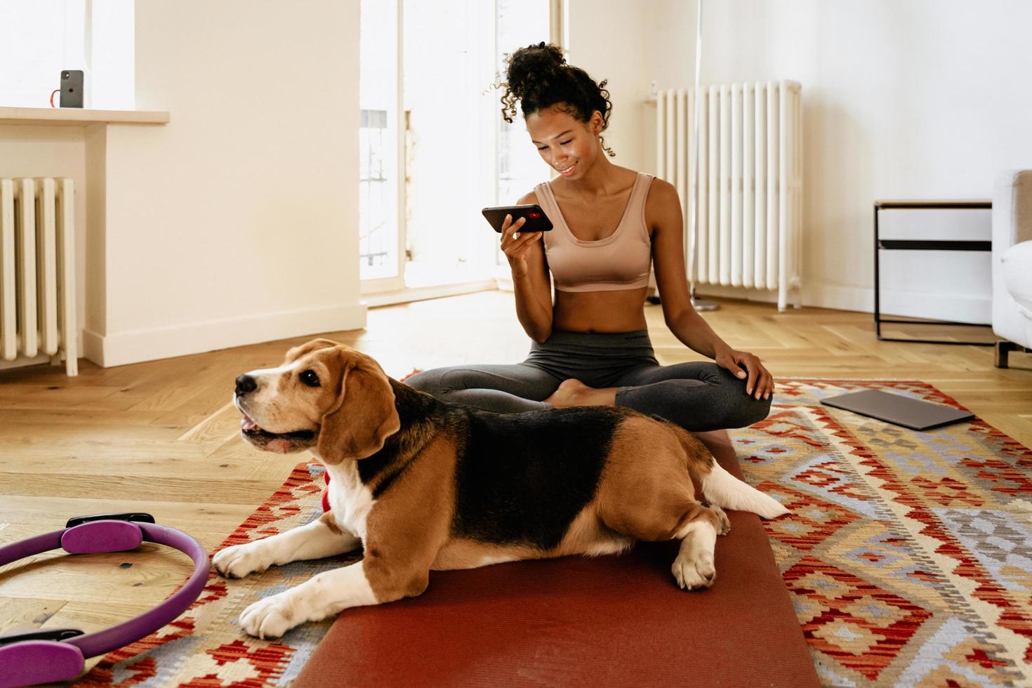 jovem negra usando o celular enquanto está sentada com seu cachorro na esteira foto