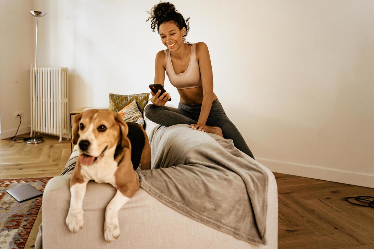 jovem negra usando o celular enquanto está sentada com o cachorro no sofá foto