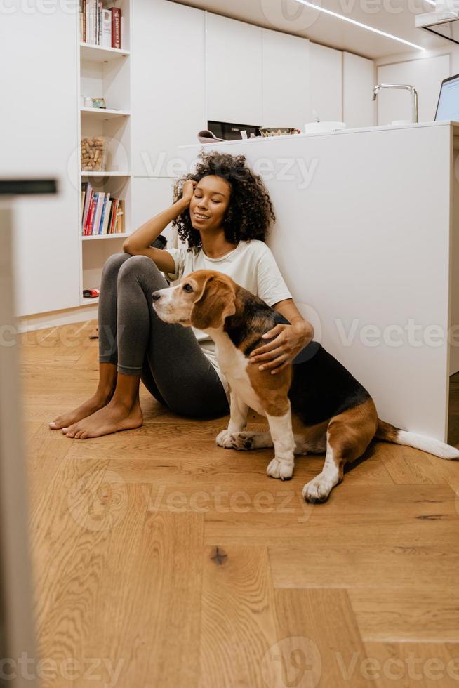 jovem negra acariciando seu cachorro enquanto está sentada no chão foto