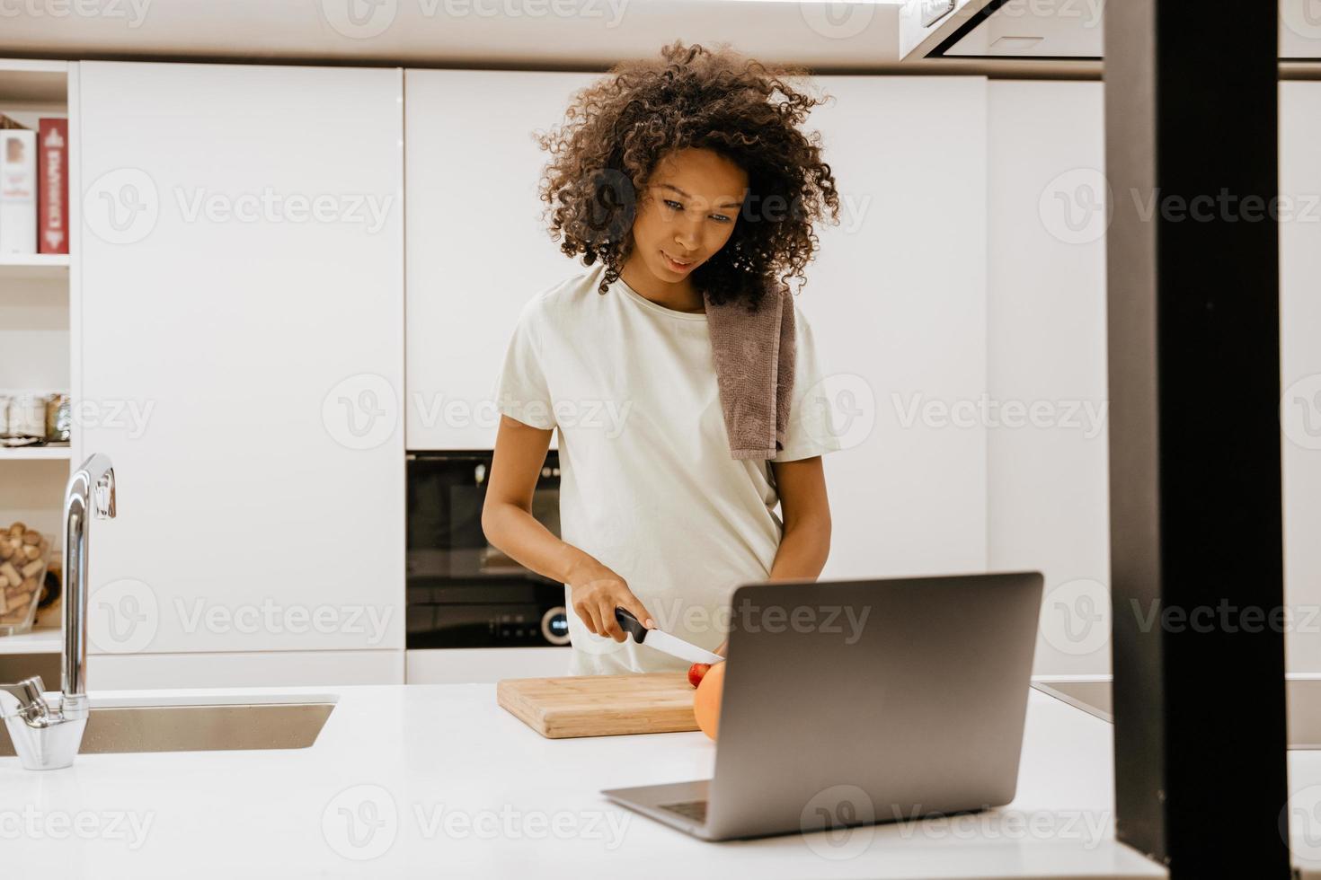 jovem negra fazendo salada enquanto usa o laptop na cozinha foto