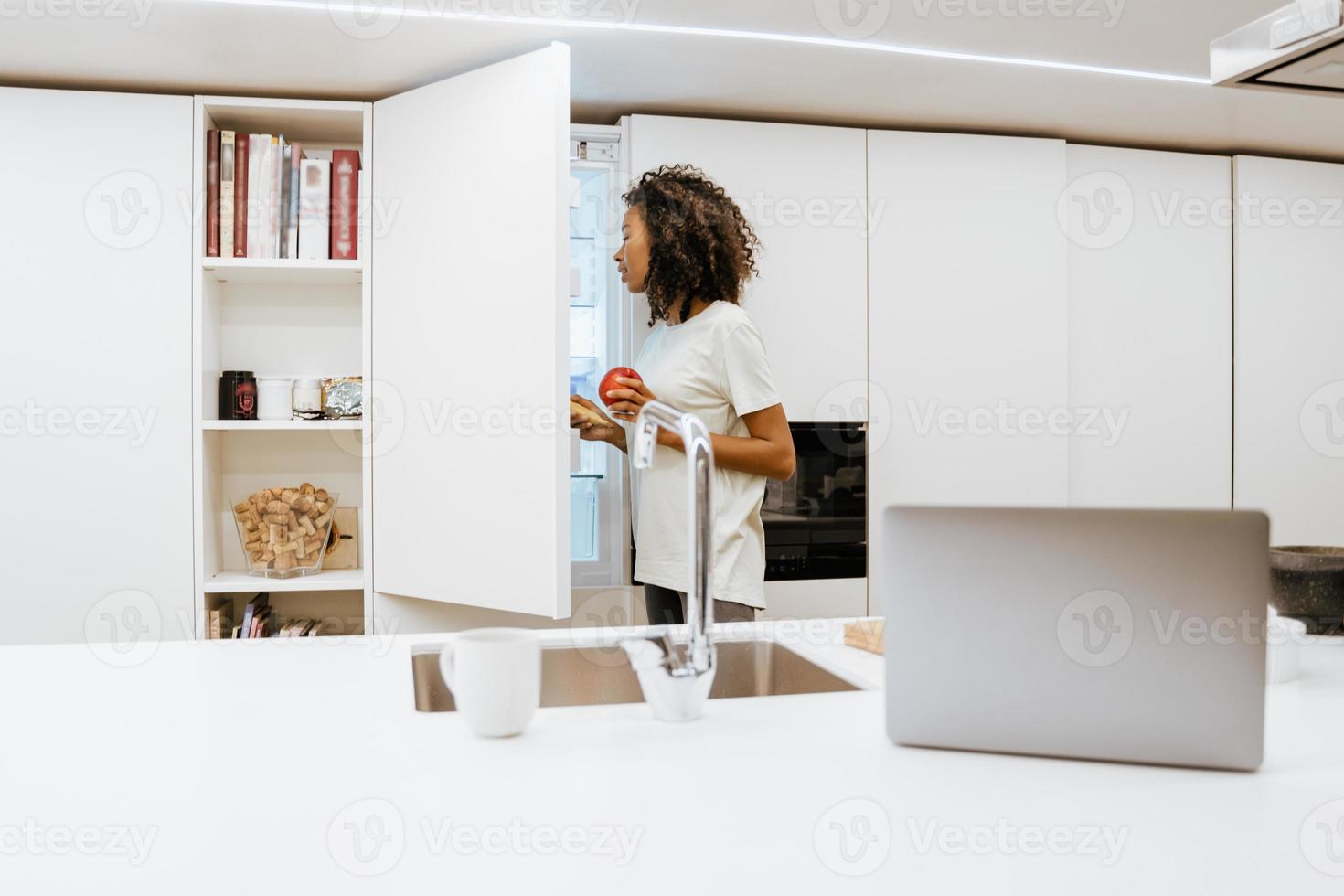 jovem negra abrindo o freezer enquanto prepara o café da manhã na cozinha foto