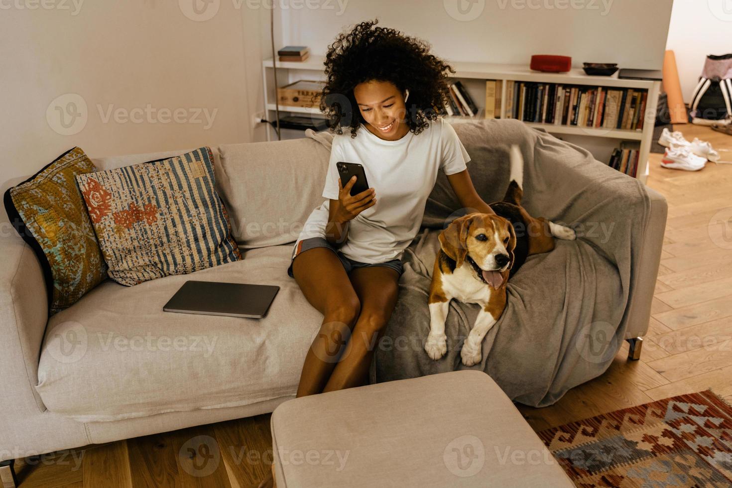 jovem negra usando o celular e acariciando o cachorro no sofá foto