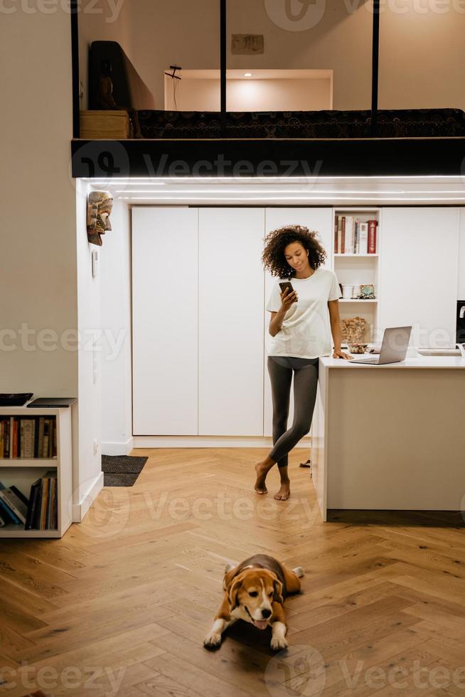 mulher negra usando celular enquanto trabalha com laptop foto