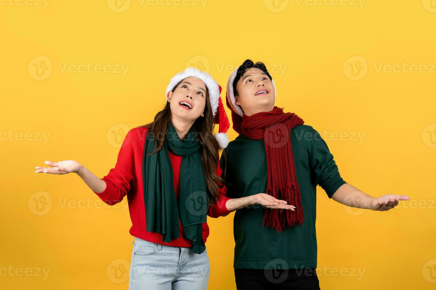 foto do a animado ásia casal dentro Natal roupas olhando acima com aberto mãos em uma amarelo estúdio fundo.