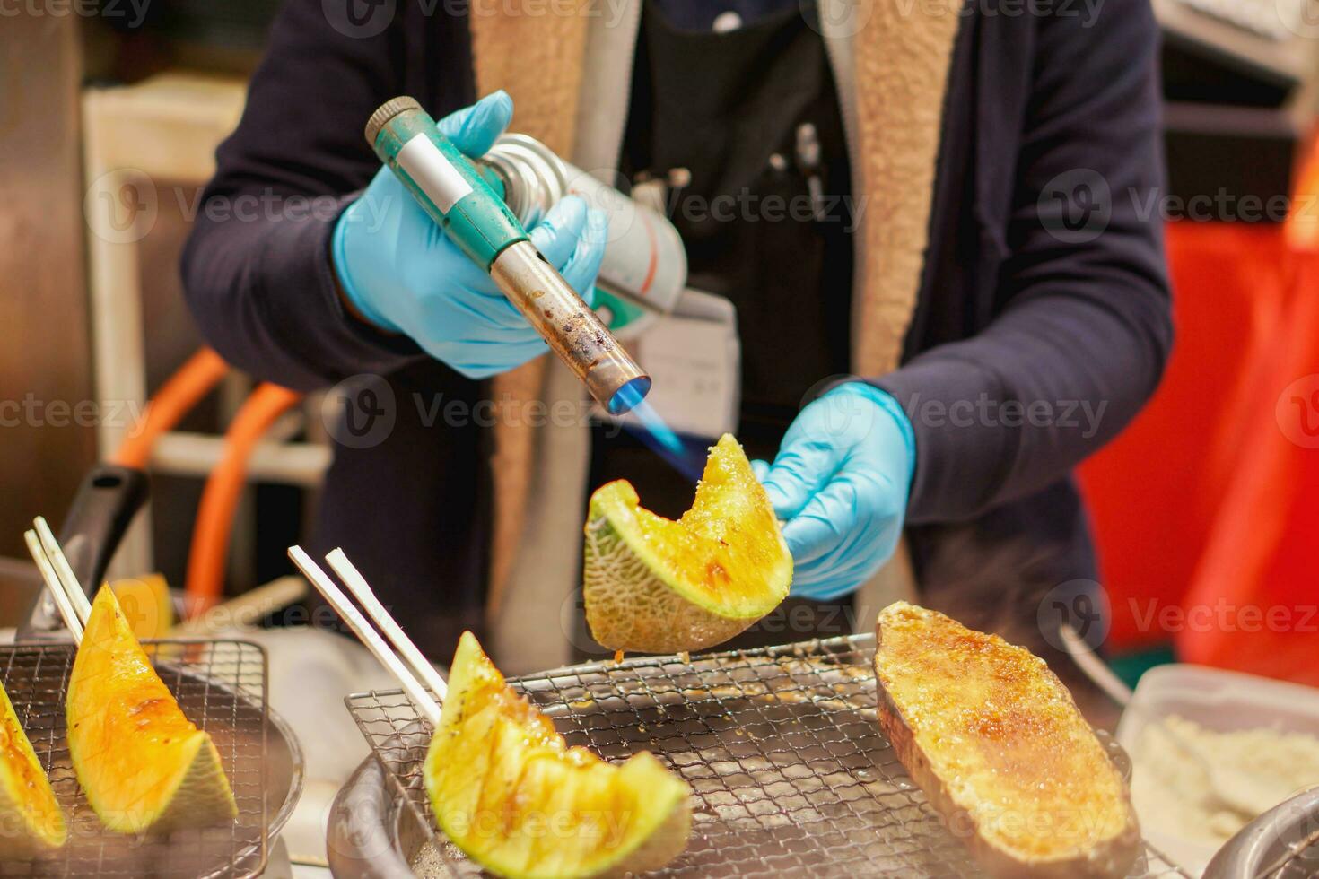 mão do chefe de cozinha usando queimador cozinhando e queimar fatia do melões e melões em fogão para venda para cliente às kuromon mercado. melões Churrasco é pitoresco e popular entre turistas quem venha para Japão. foto