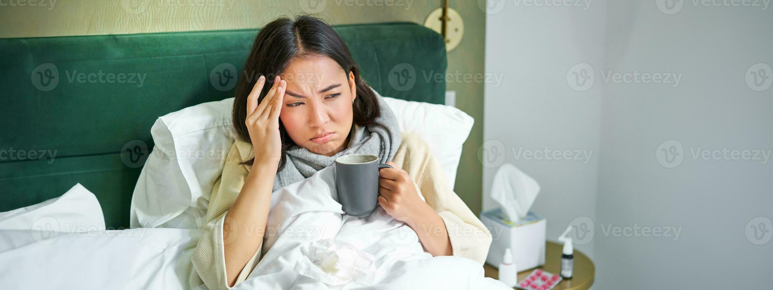 gripe, doença e pessoas. jovem mulher sentindo-me doente, tendo febre e pegando col, deitado dentro cama com quente chá, levando drogas a partir de gripe foto
