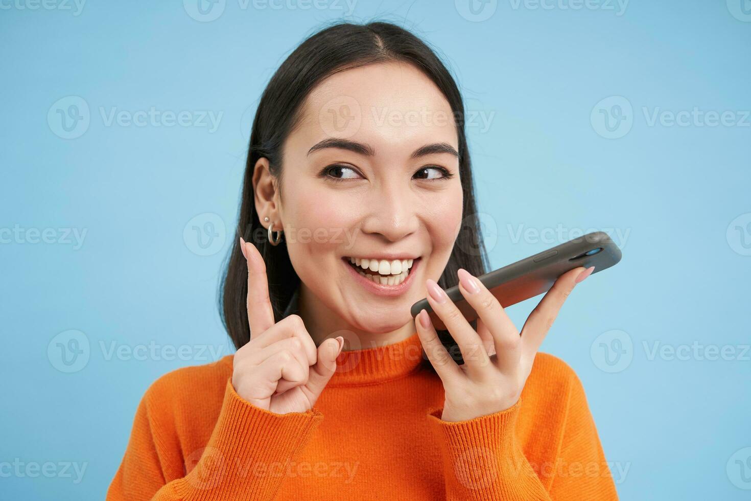 retrato do coreano mulher registros voz mensagem em Smartphone aplicativo, fala em palestrante, traduz dela discurso em Móvel aplicativo, azul fundo foto