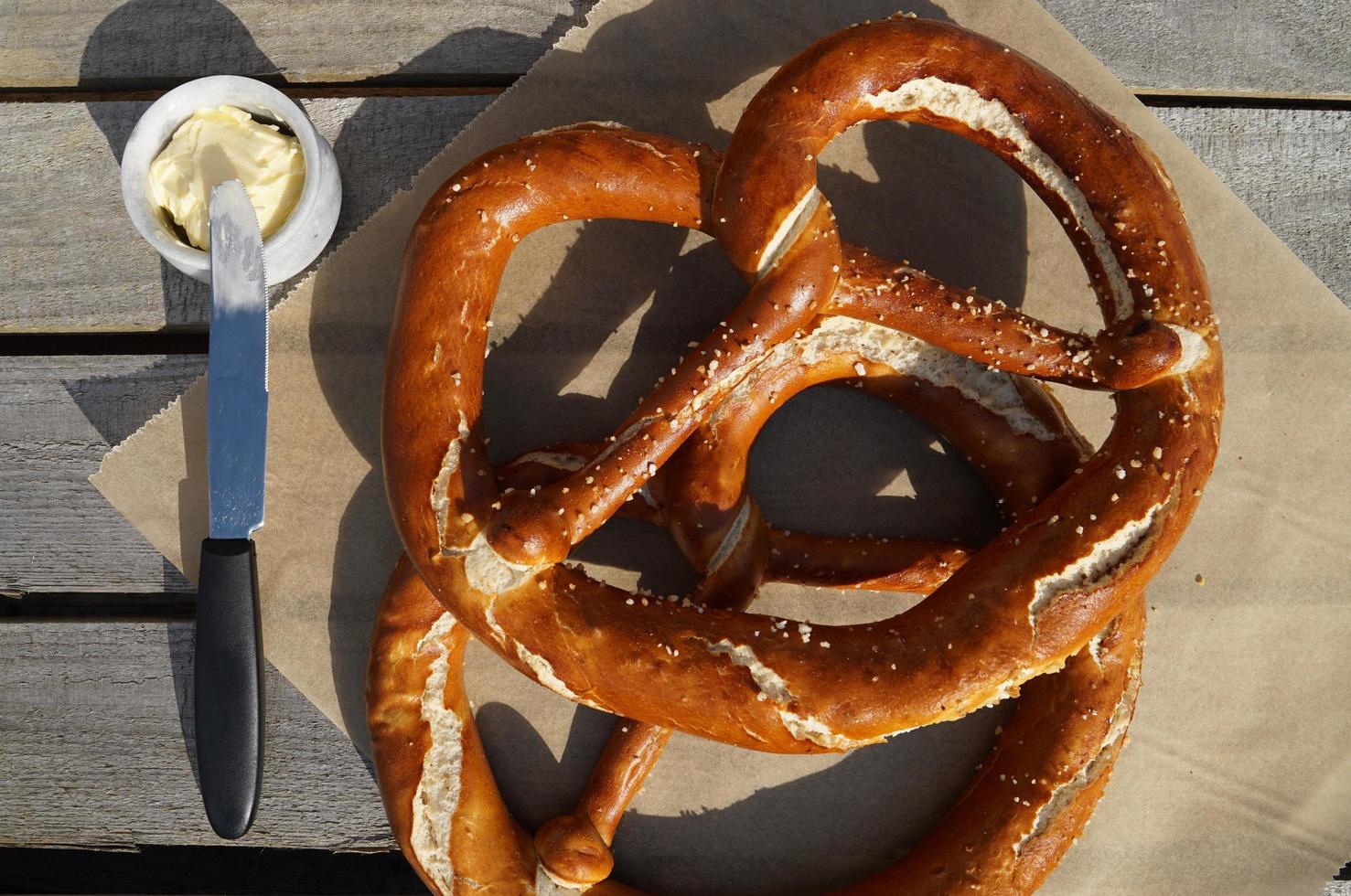 grande pretzel, manteiga e faca na mesa de madeira no jardim. foto