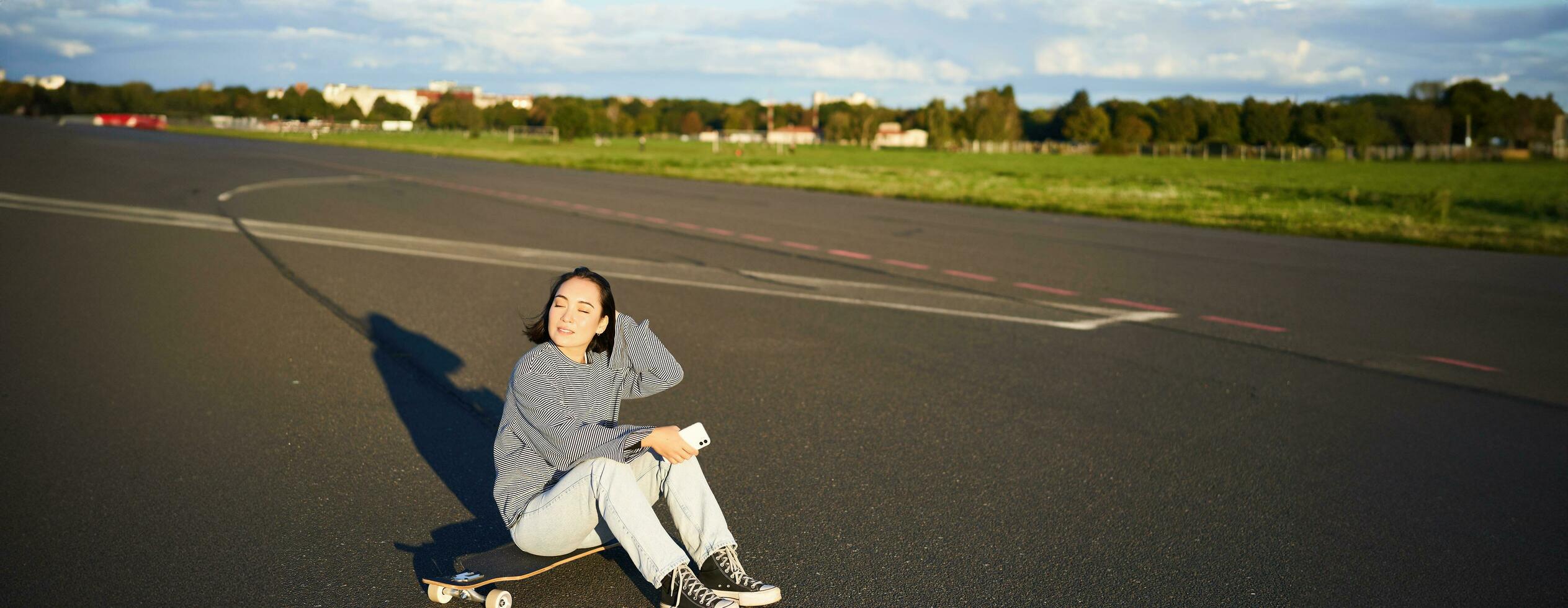 skatista menina senta em dela skate em estrada, usando Smartphone, conversando em Móvel aplicativo foto