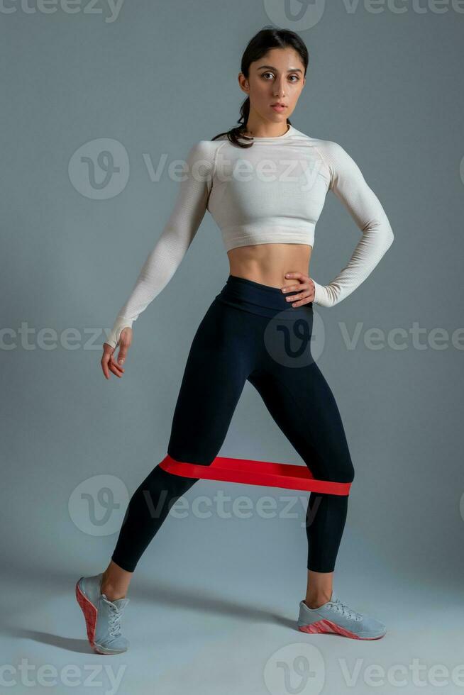 menina fazendo mais baixo corpo exercícios com resistência banda em cinzento fundo foto