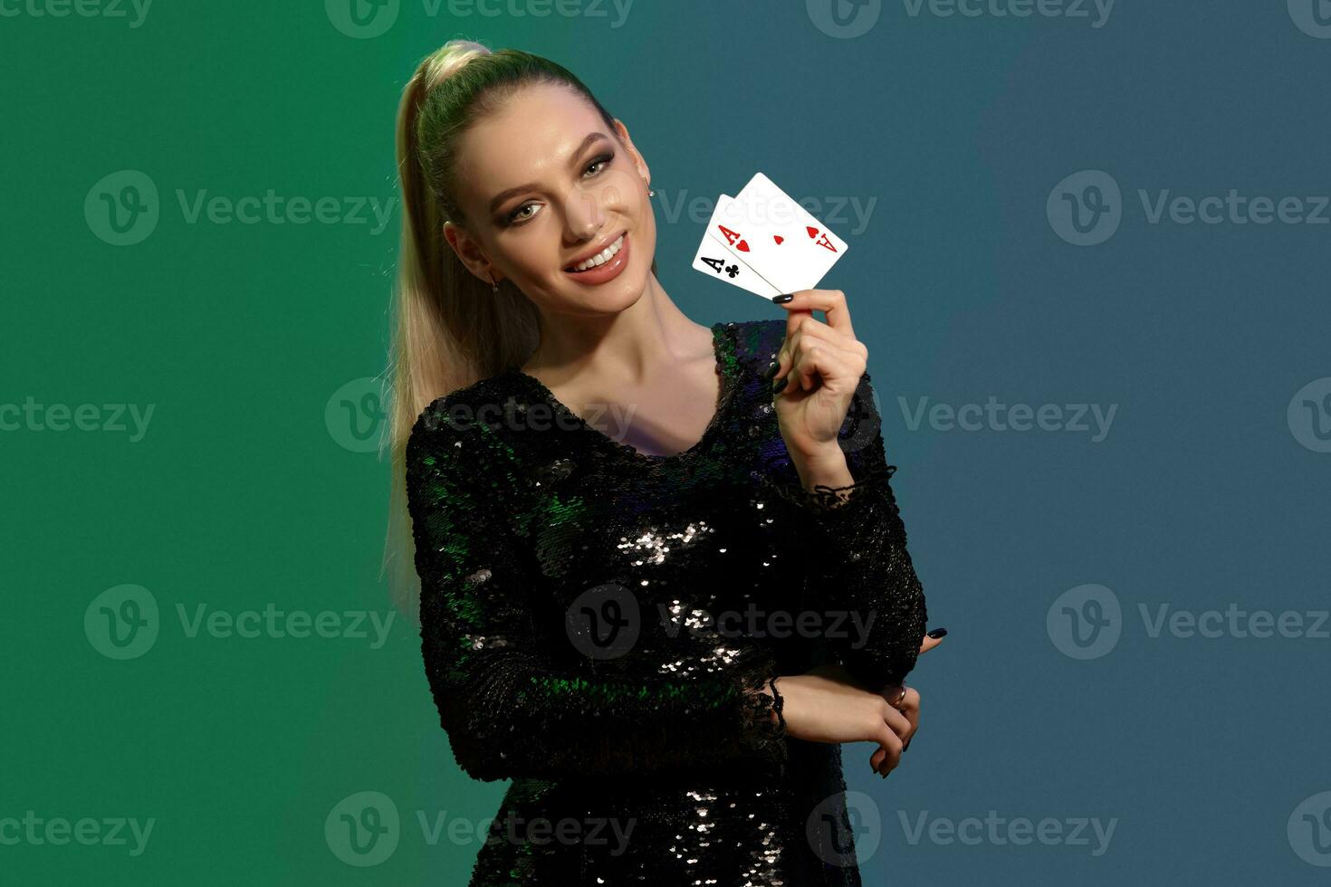 Loiras fêmea dentro joalheria e Preto lantejoulas vestir. ela sorridente, mostrando dois jogando cartões, posando em colorida fundo. pôquer, casino. fechar-se foto