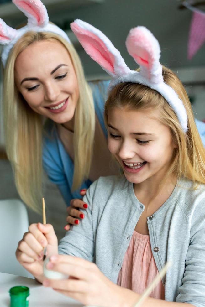 sorrindo, mãe e filha pintam ovos de Páscoa em orelhas de coelho. foto