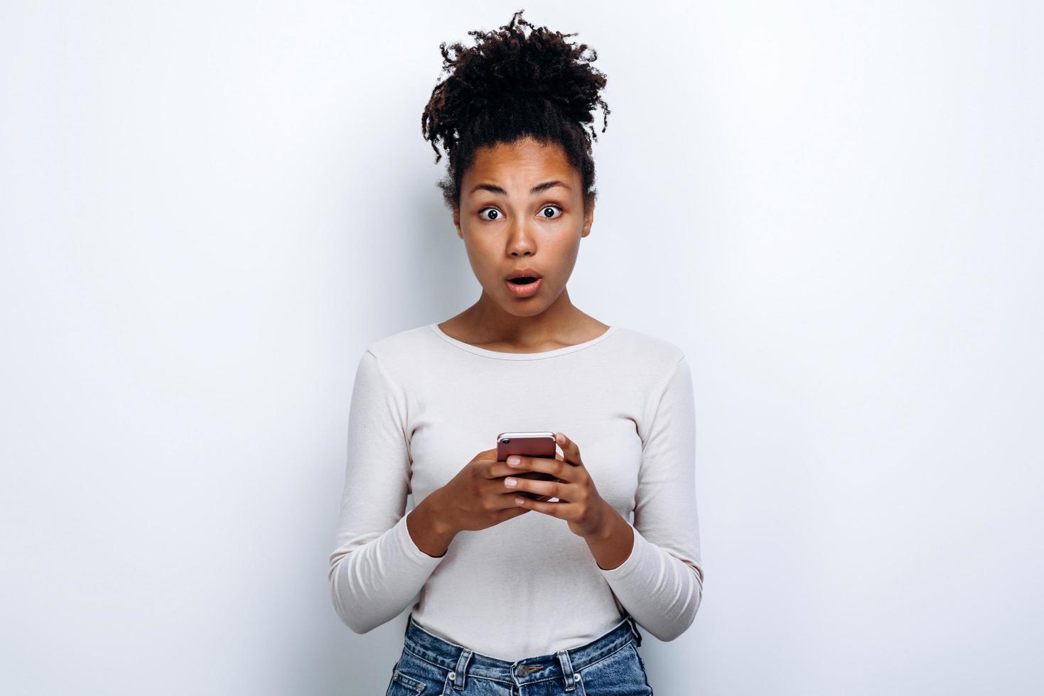 garota surpresa com um telefone nas mãos do estúdio com um fundo branco foto