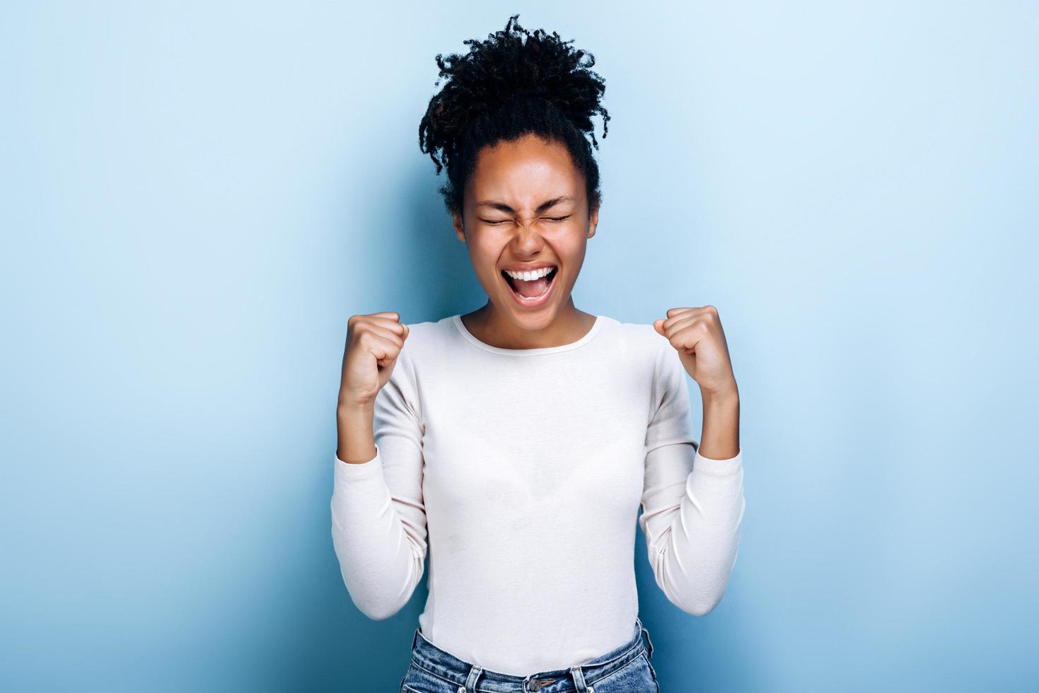 jovem africana feliz fazendo gesto de vencedor posando isolado sobre fundo azul foto