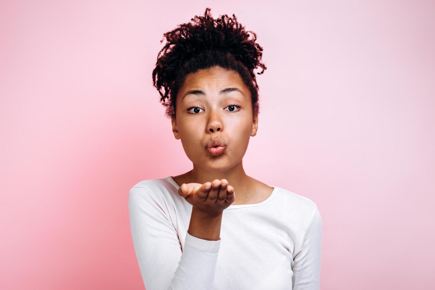 feche o retrato de uma mulher linda e encantadora atraente, ela está mandando um beijo no ar, isolado em um fundo rosa brilhante foto