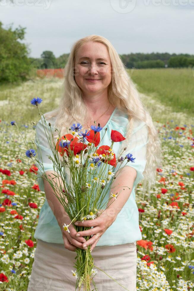 lindo meia idade Loiras mulher carrinhos entre uma floração campo do papoilas foto