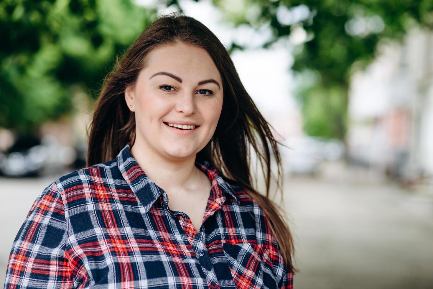 Mulher bonita sorridente olhando direto para a câmera na rua debaixo de uma árvore verde foto