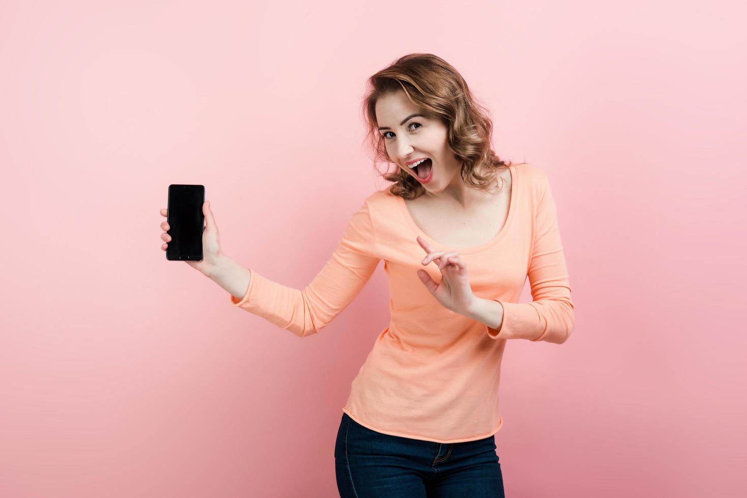 garota feliz e animada segurando um smarphone na mão e olhando para a câmera foto