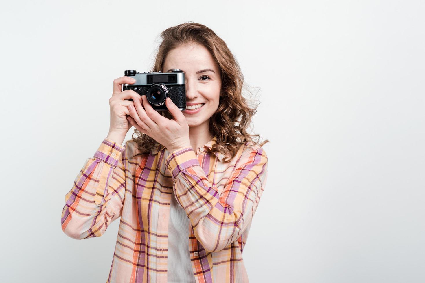 retrato de uma garota feliz usando uma câmera retro sobre o fundo branco do estúdio foto