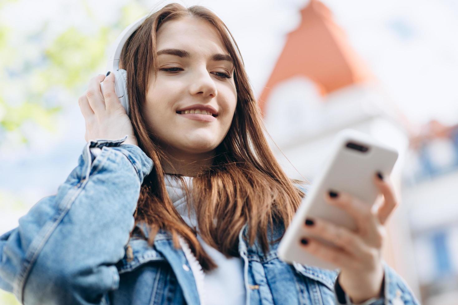 garota atraente com cabelo escuro e fones de ouvido, olhando algo no telefone foto