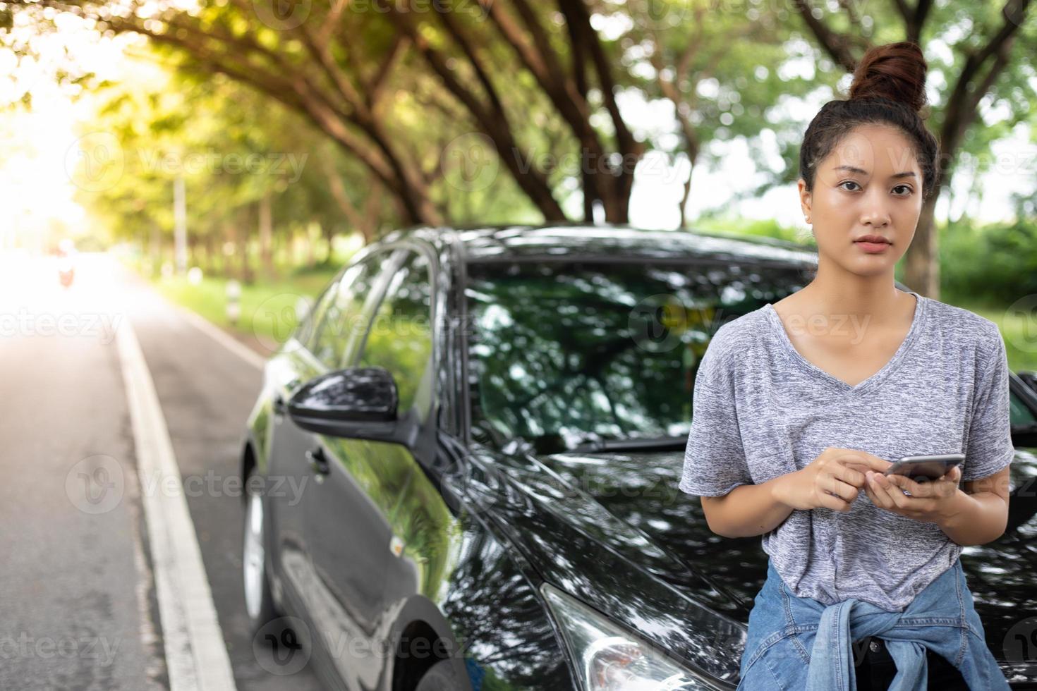 Mulher asiática usando telefone celular enquanto olha e homem estressado sentado após uma quebra de carro na rua foto