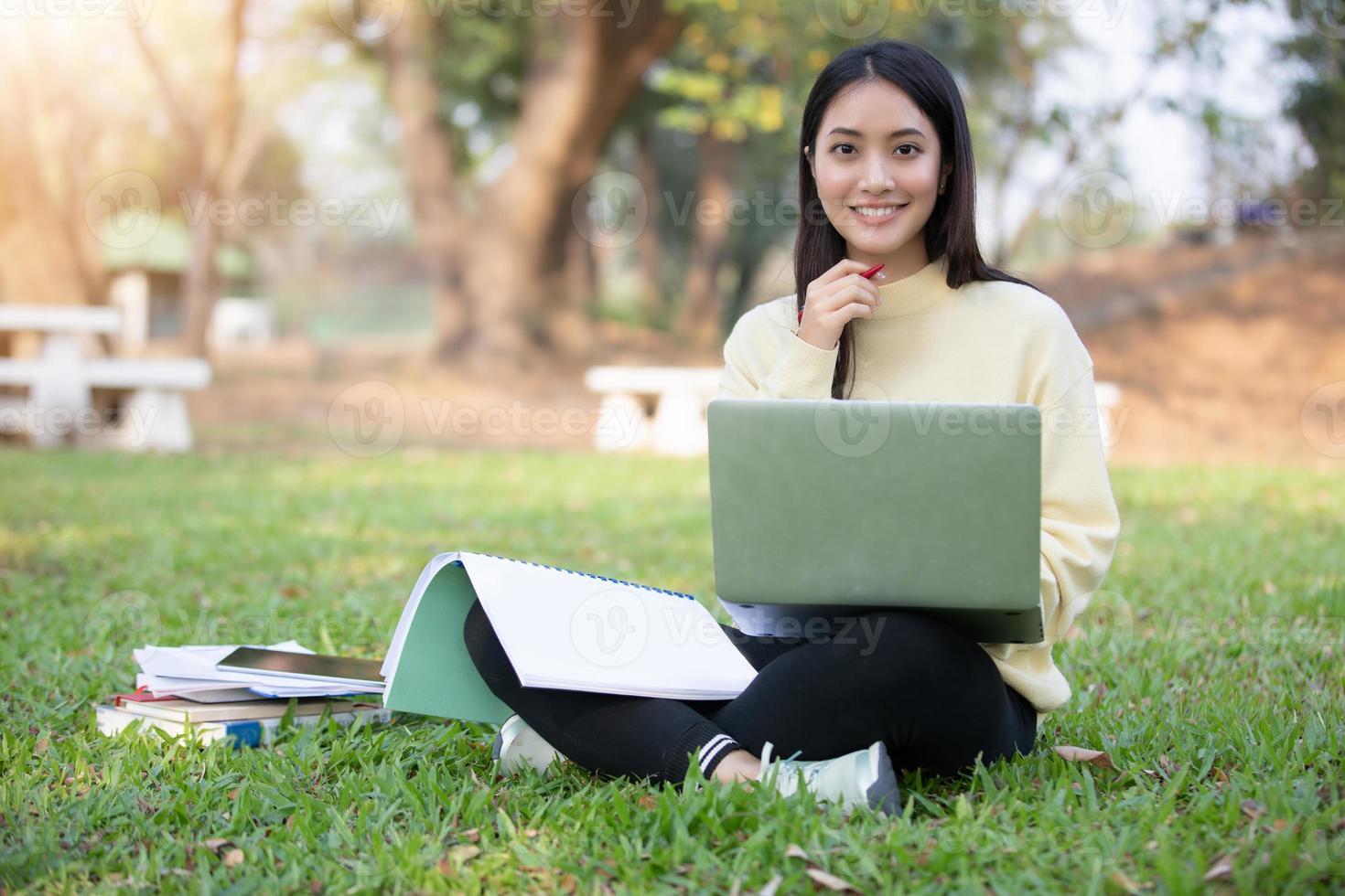 estudantes universitários de mulheres asiáticas sorrindo e sentados na grama verde trabalhando e lendo juntos em um parque. foto