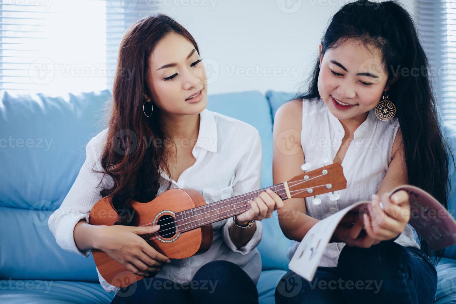 duas mulheres asiáticas se divertindo tocando cavaquinho e sorrindo em casa para relaxar foto