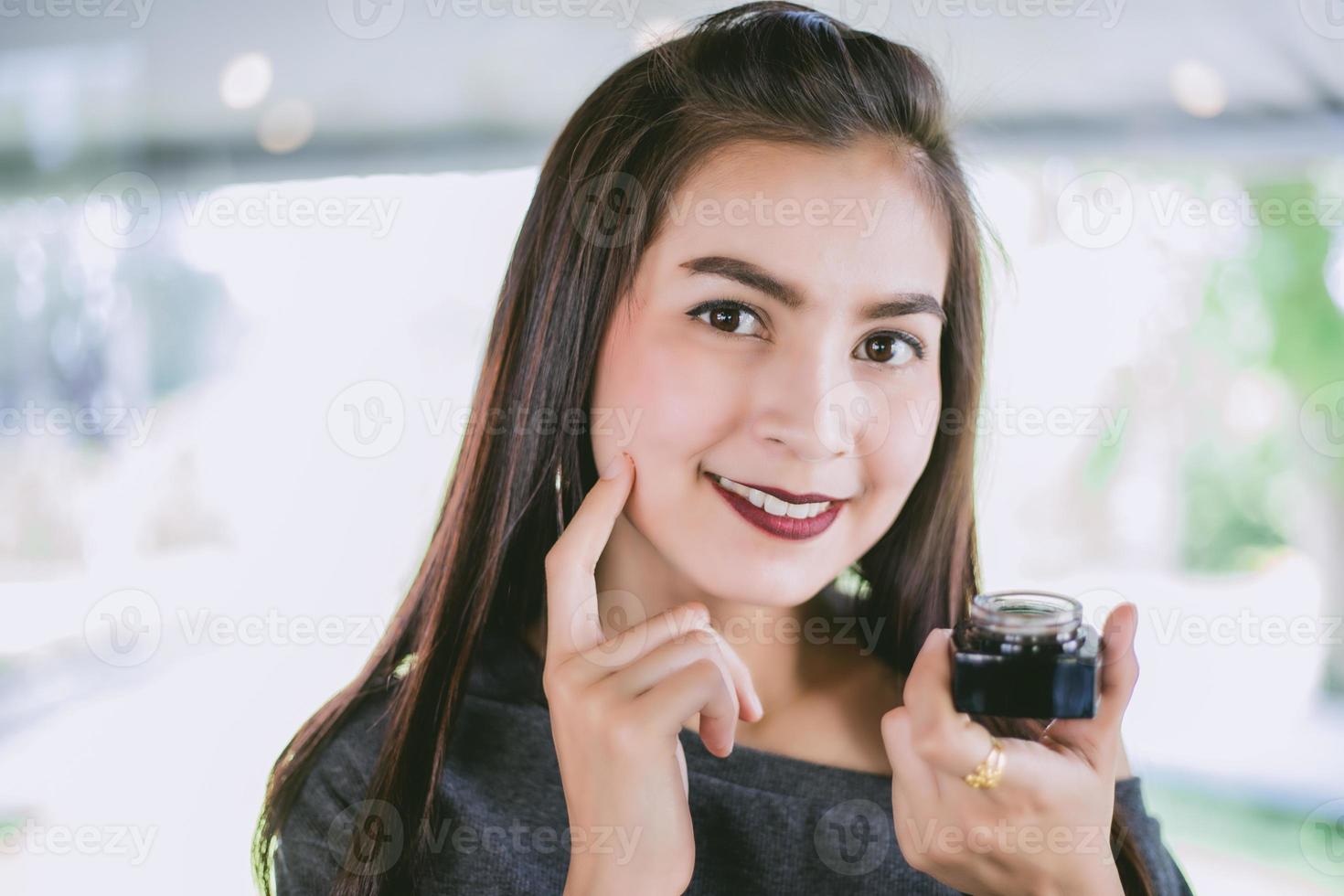 uma linda mulher asiática usando um produto para a pele, hidratante ou loção para cuidar de sua pele seca. creme hidratante nas mãos femininas. foto