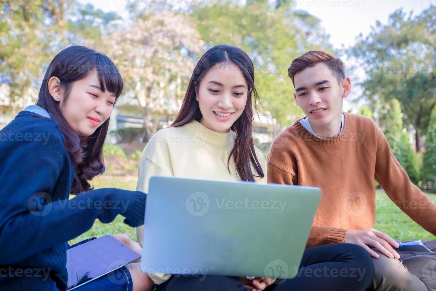 grupo de estudantes universitários asiáticos sentados na grama verde trabalhando e lendo juntos em um parque foto