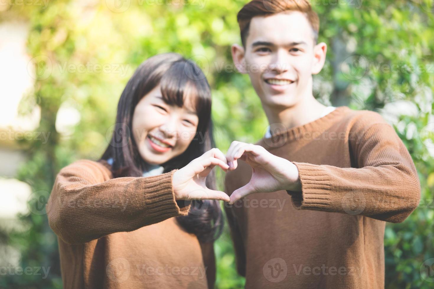 lindo casal jovem fazendo formato de coração com as mãos e sorrindo feliz e apaixonado ao ar livre foto