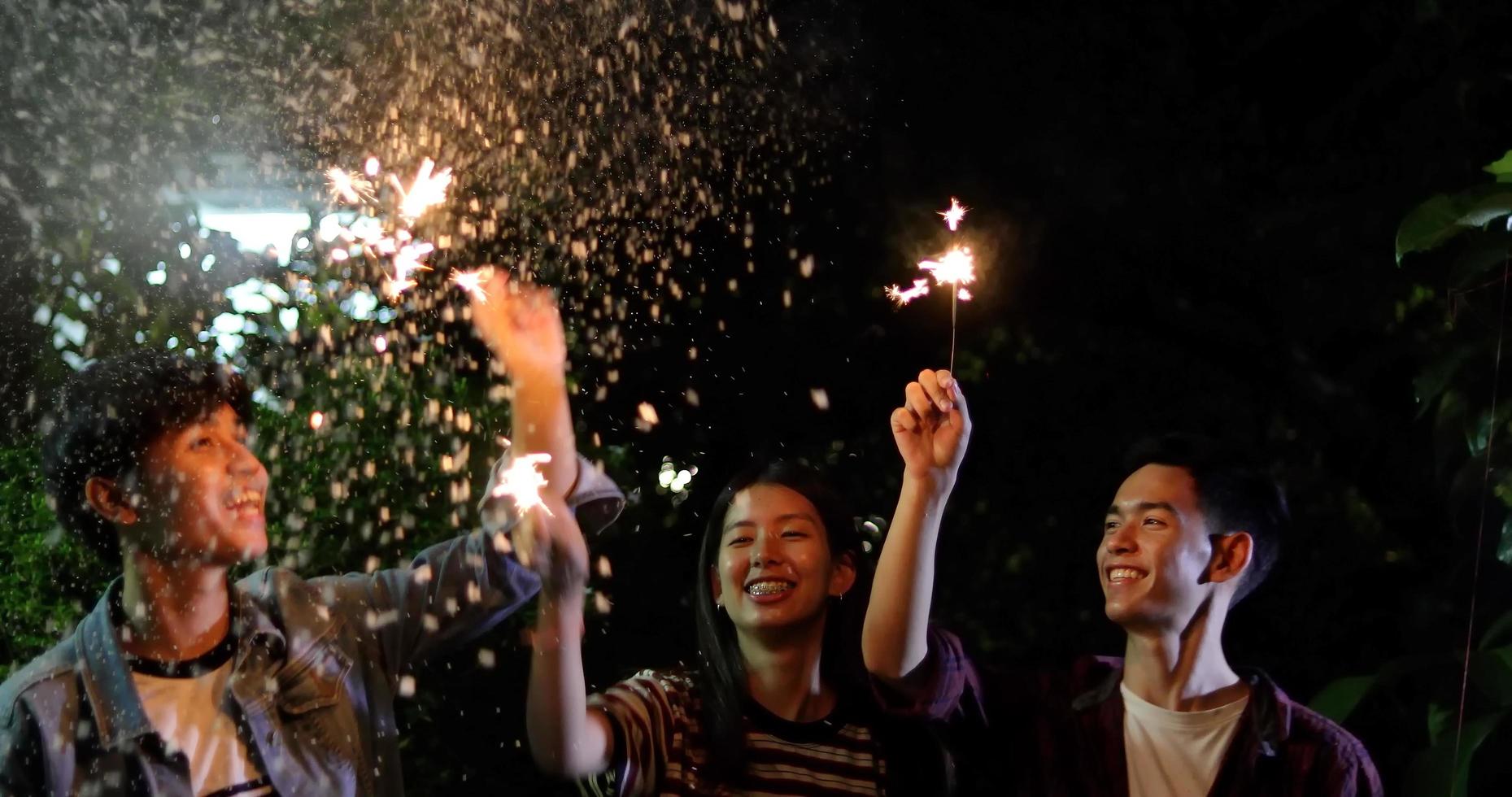 Grupo asiático de amigos fazendo churrasco ao ar livre no jardim, rindo com bebidas alcoólicas de cerveja e mostrando um grupo de amigos se divertindo com estrelinhas à noite, foco suave foto