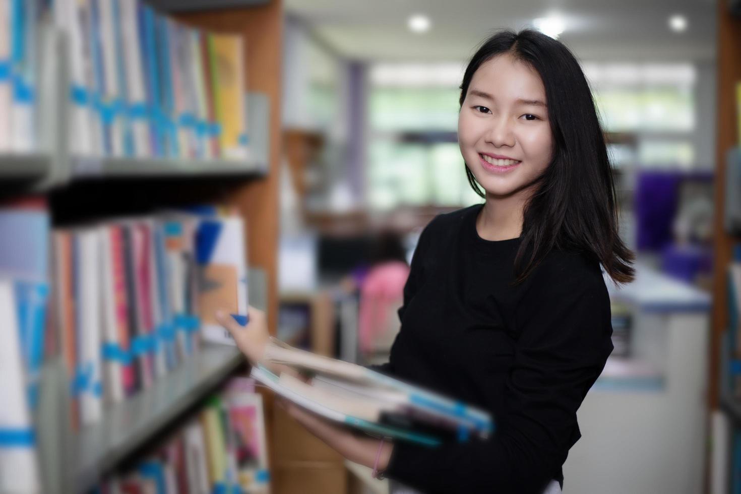 Alunos asiáticos segurando um livro de seleção na biblioteca foto