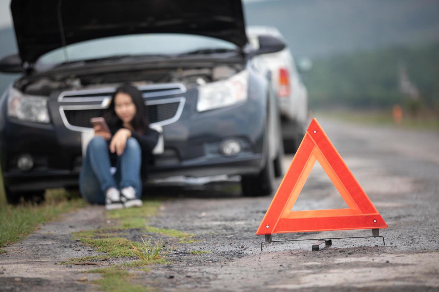 Mulher asiática usando telefone celular enquanto olha e homem estressado sentado após uma quebra de carro na rua foto