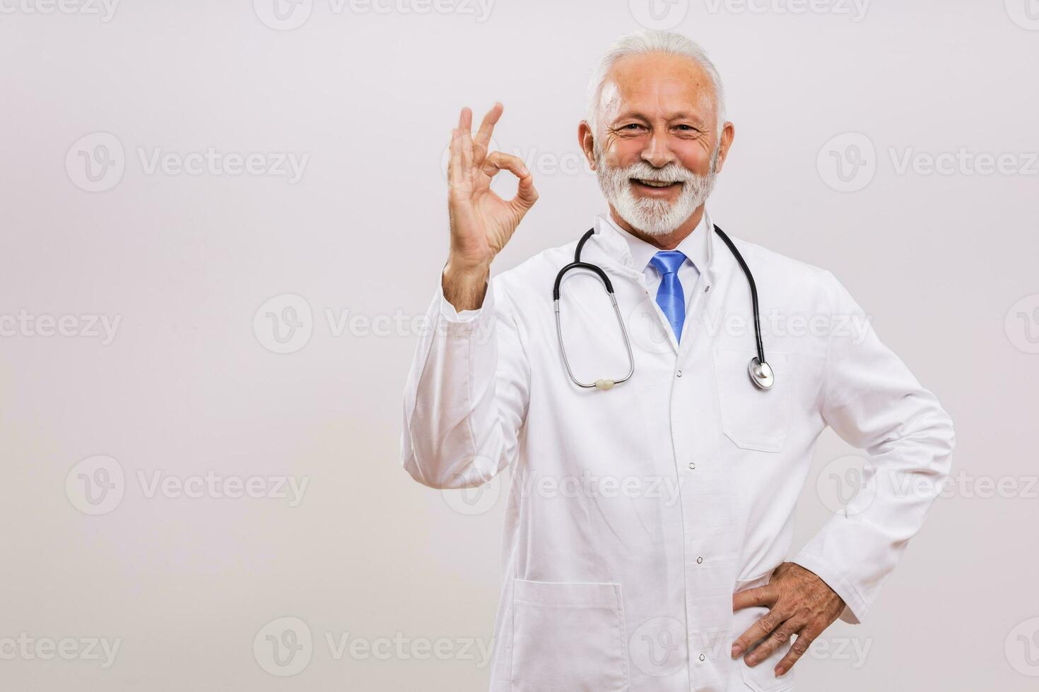 retrato do Senior médico mostrando Está bem placa em cinzento fundo. foto