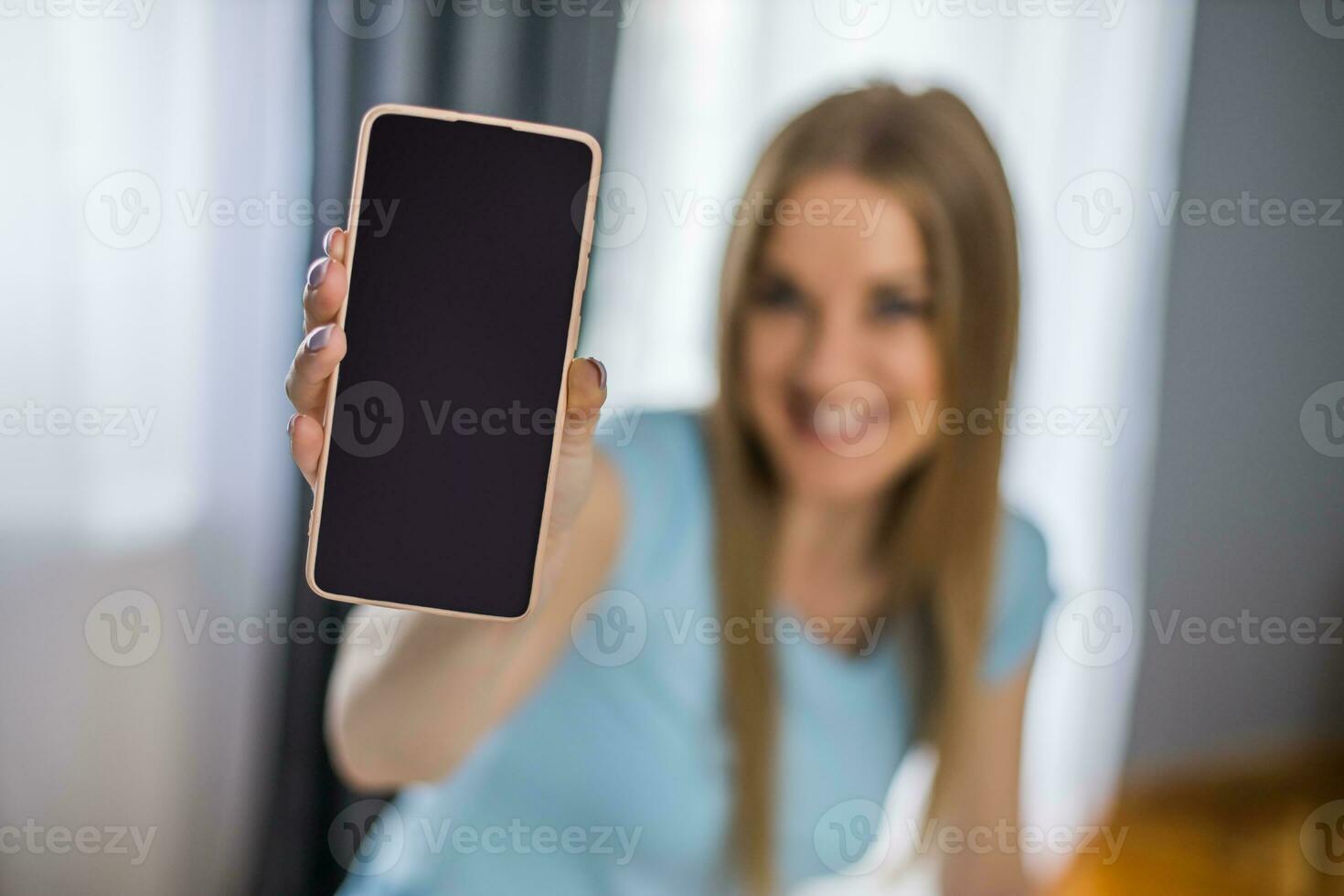 jovem mulher segurando Móvel telefone com em branco tela para seu advertir. foco em telefone. foto