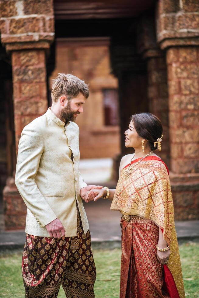 Noiva asiática e noivo caucasiano se divertindo com um vestido tailandês foto