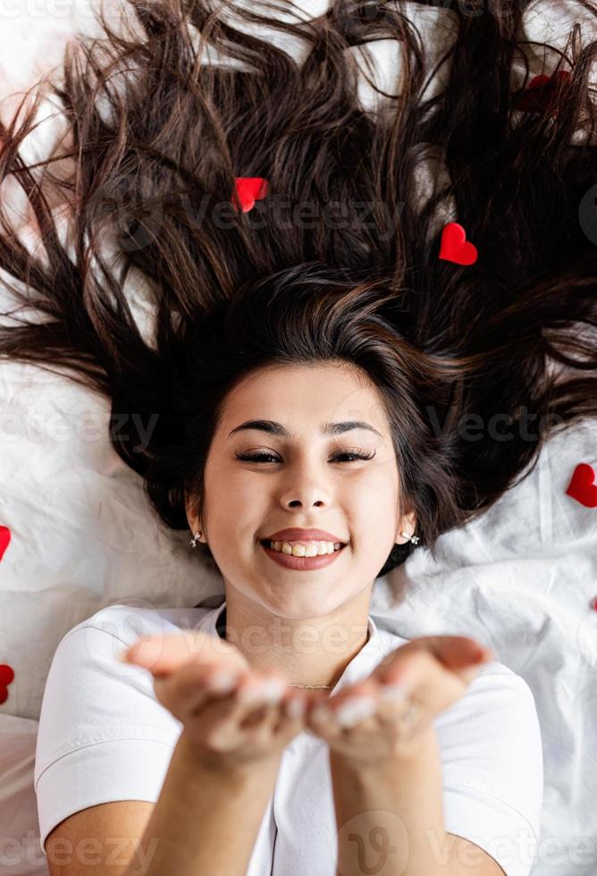 jovem morena feliz deitada na cama mandando um beijo foto