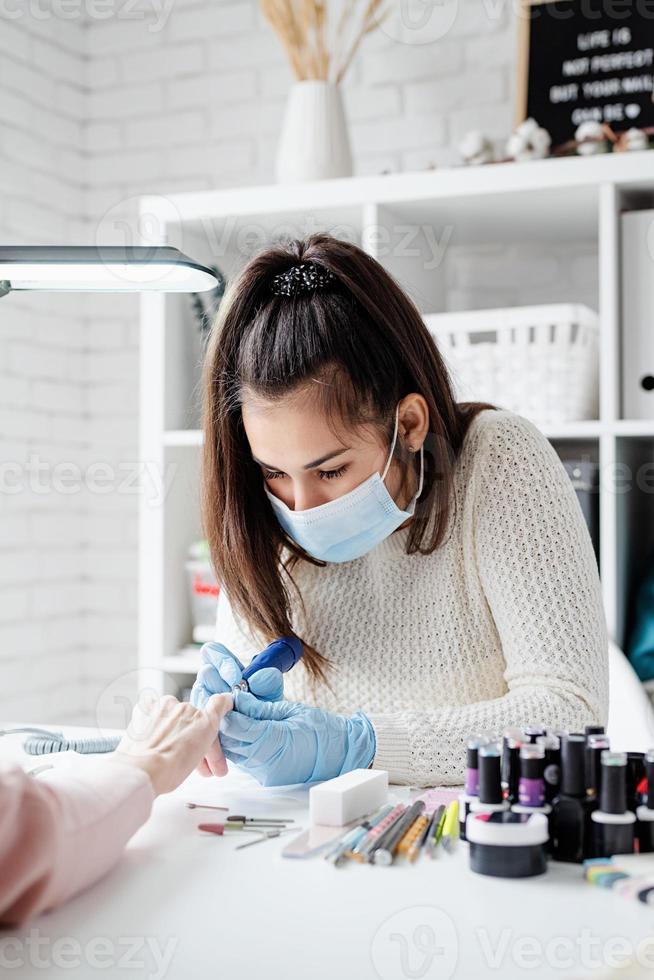 mestre de manicure usando uma máquina elétrica para remover o esmalte durante a manicure no salão foto