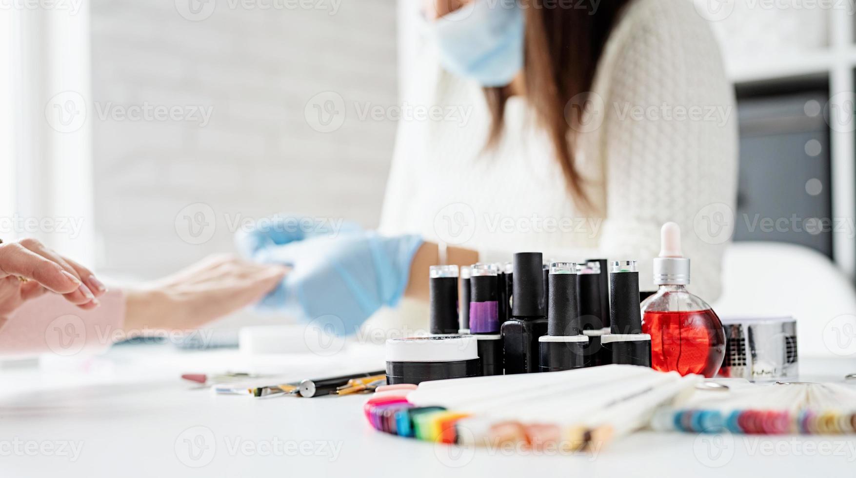 mestre de manicure com luvas de borracha e máscara conversando com a cliente no interior do estúdio de beleza foto