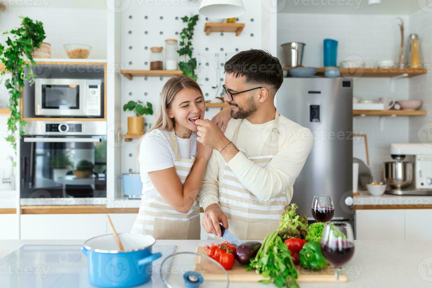 jovem casal é olhando às cada de outros e alimentando cada de outros com sorrisos enquanto cozinhando dentro cozinha às lar. amoroso alegre jovem casal abraçando e cozinhando junto, tendo Diversão dentro a cozinha foto