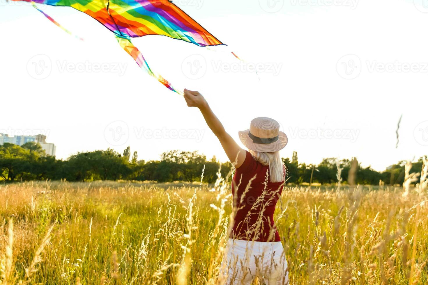 beleza menina corrida com pipa em a campo. lindo jovem mulher com vôo colorida pipa sobre Claro azul céu. livre, liberdade conceito. emoções, saudável estilo de vida foto